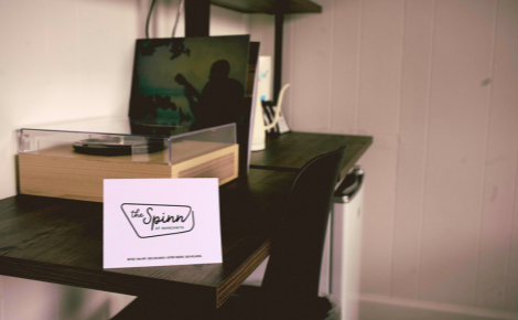 small wooden desk with a record player and records propped up in background with a white tent card showing The Spinn at Manzanita logo in front.